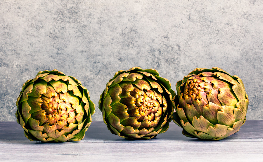 still life of three artichokes on a wood table