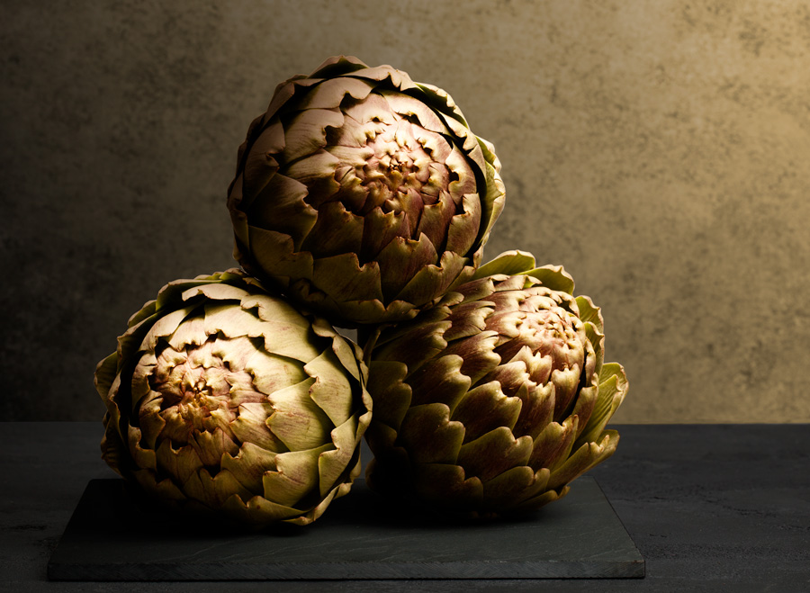 three artichokes on a slate surface